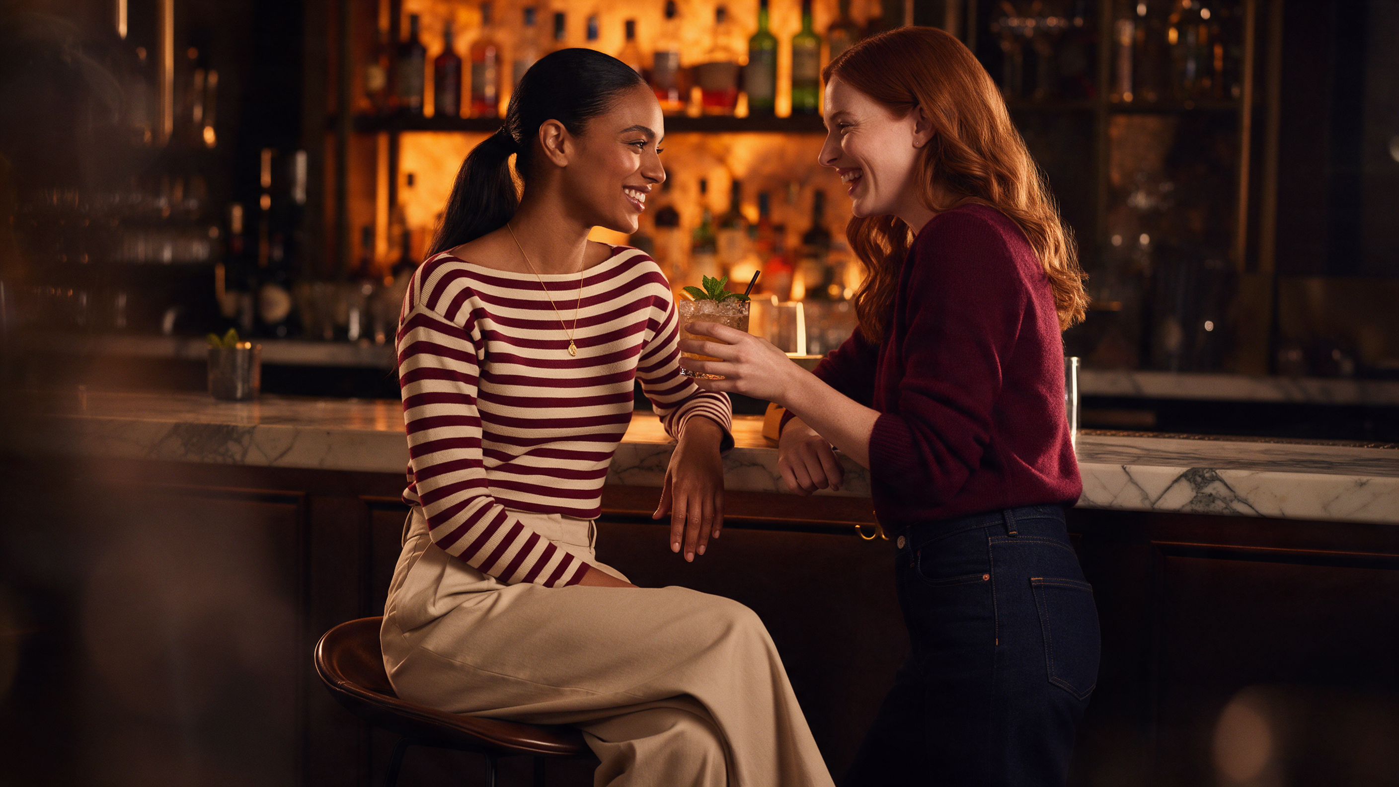 Restaurant date outfit 2026: woman wearing a burgundy striped boat neck knit sweater with neutral tailored bottoms and gold earrings