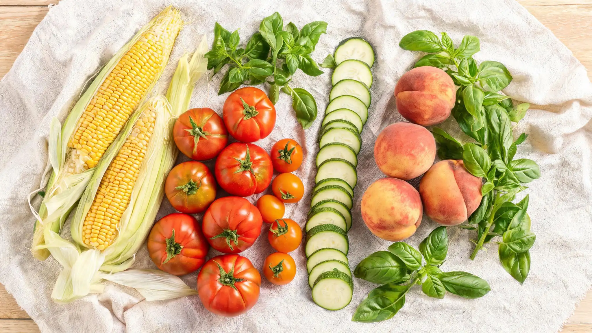 Late summer produce flat lay with corn, tomatoes, zucchini, peaches, and basil