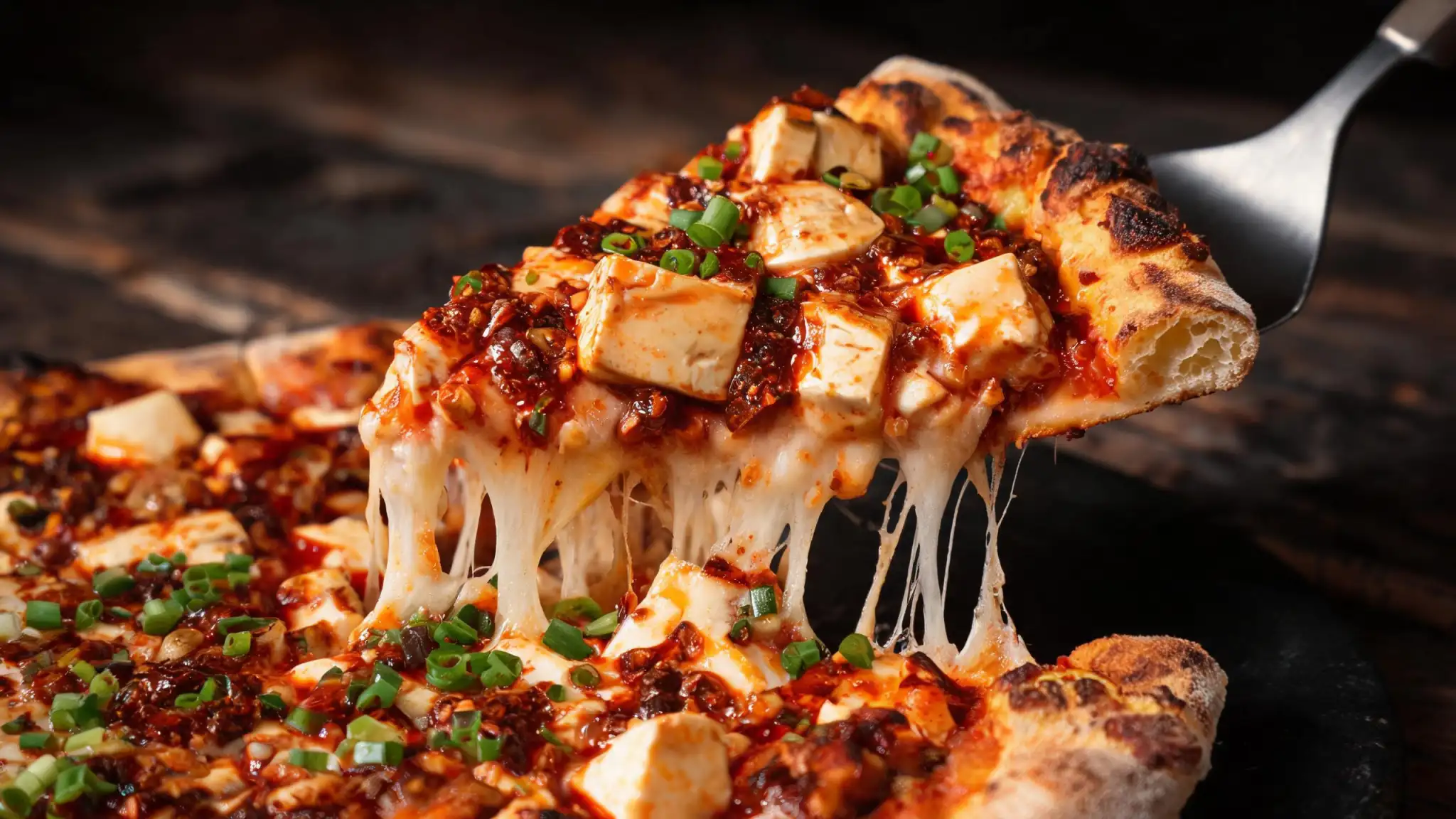Mapo tofu pizza slice with a cheese pull, glossy red mala topping